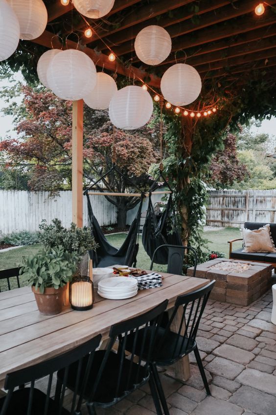 an outdoor dining area with hanging lanterns and potted plants on the table in front of it