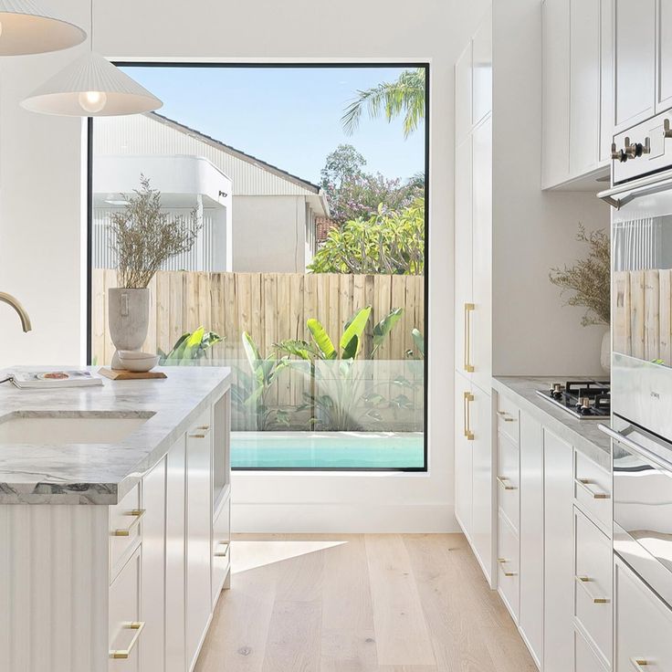 a kitchen with white cabinets and an open window that looks out onto the pool outside