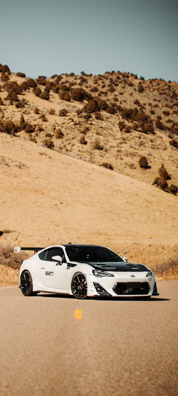 a white car is parked on the side of the road in front of some hills