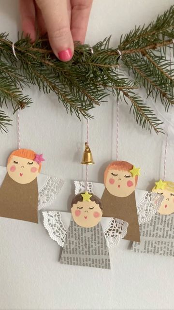 an ornament hanging from a christmas tree with three angels on it and a hand holding