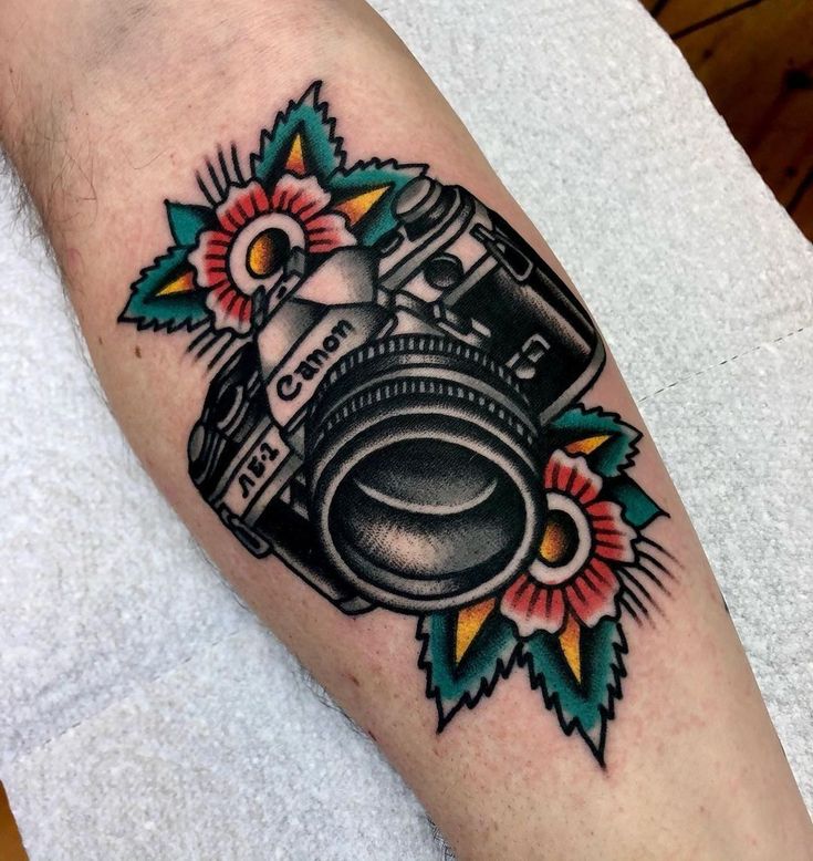 a camera tattoo on the left arm with flowers and leaves around it's edges