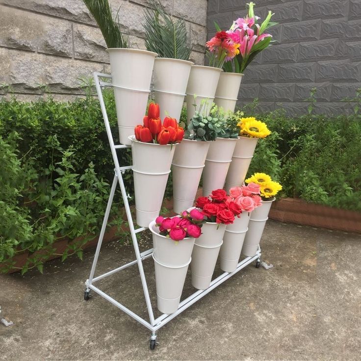 there are many flowers that are in the vases on this metal stand, which is leaning against a brick wall