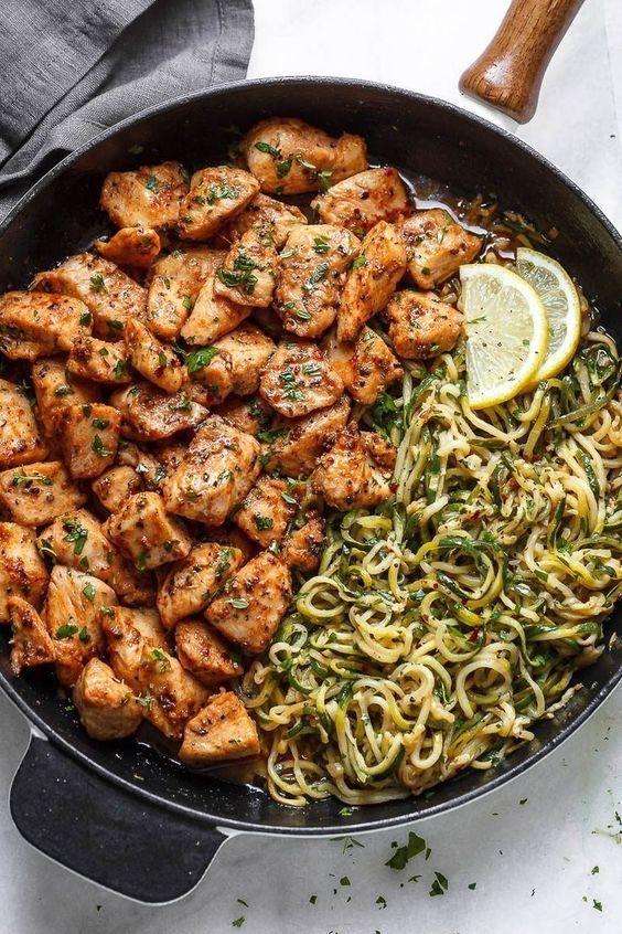 chicken and pasta in a skillet with lemon wedges