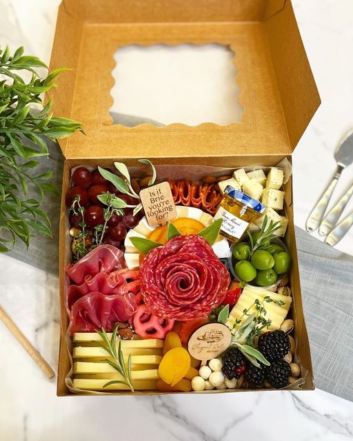 a wooden box filled with assorted cheese and meats next to a potted plant