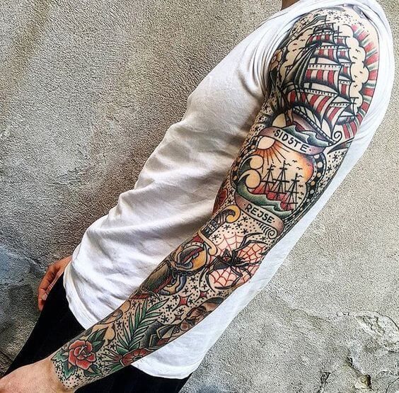 a man with a tattoo on his arm standing next to a wall and looking at the camera