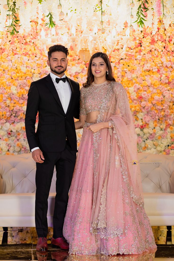 two people standing next to each other in front of a wall with flowers on it