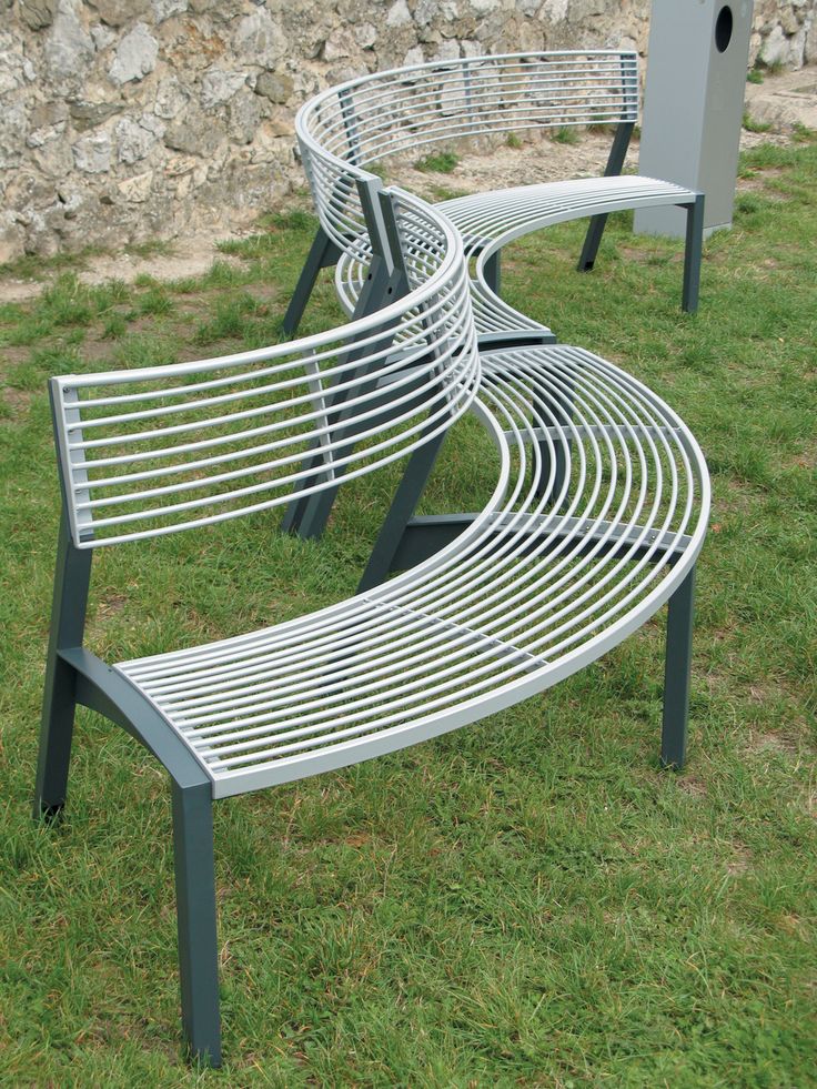 two metal benches sitting on top of a grass covered park bench next to a stone wall