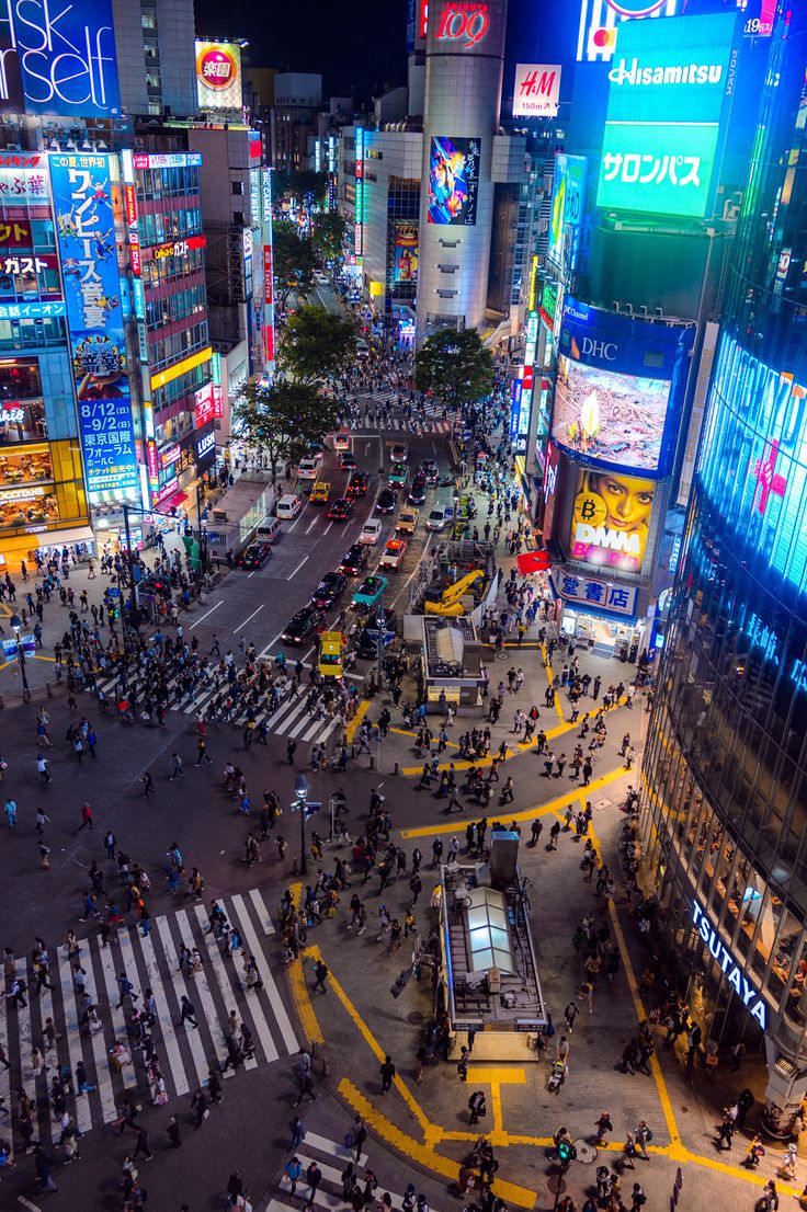 an aerial view of a city at night with many people crossing the street and buildings lit up