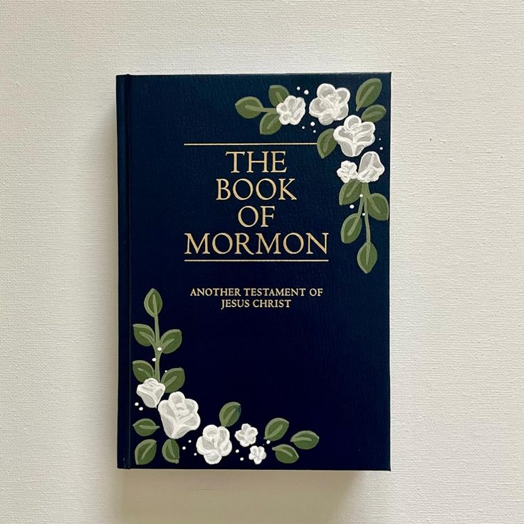 the book of mormon with white flowers and green leaves on blue cover against a white wall