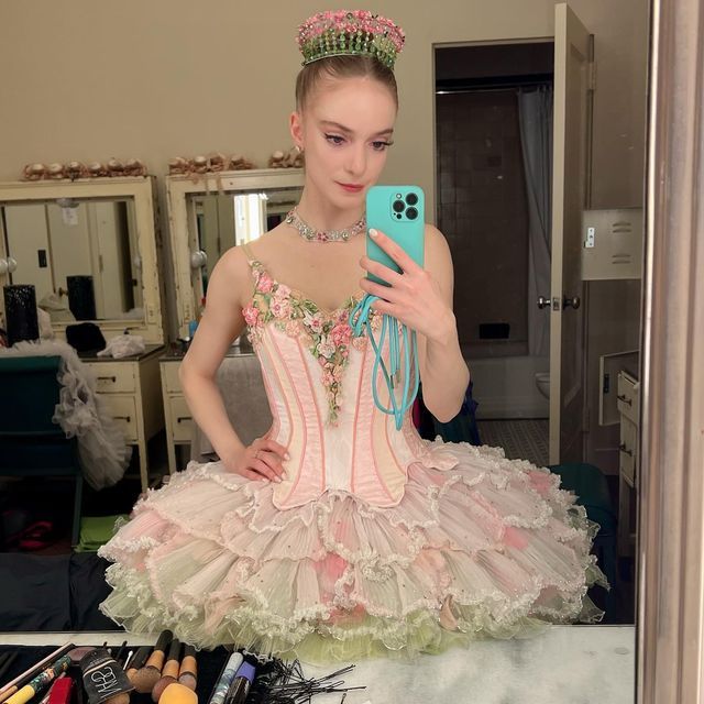 a woman in a pink and white dress holding a cell phone while wearing a tiara