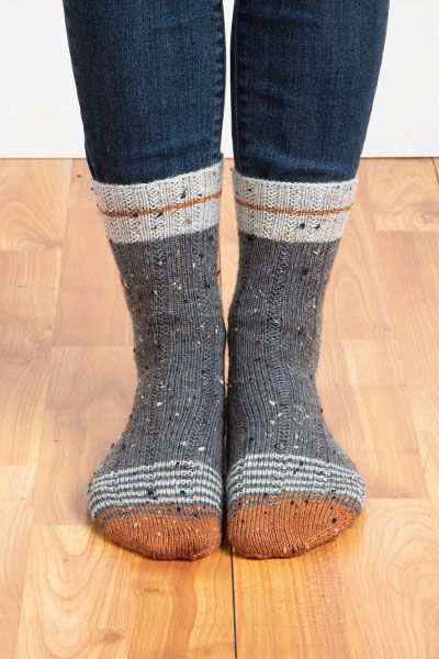 a person standing on top of a wooden floor wearing gray socks with white and grey stripes