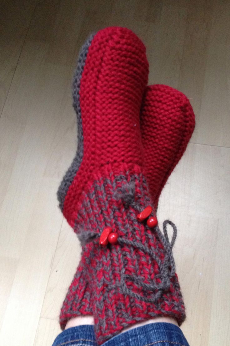 someone's feet wearing red and grey knitted mittens on the floor with their legs crossed