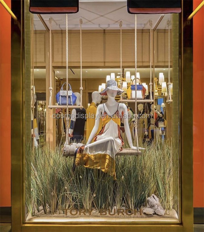 a window display with mannequins dressed in white and gold sitting on grass