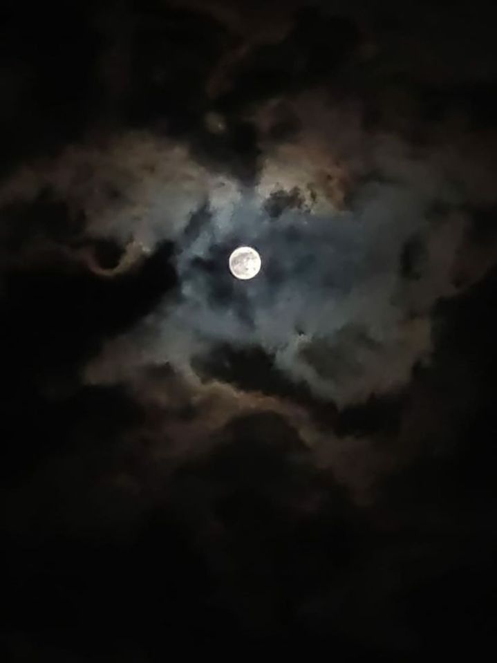 the moon is shining brightly in the dark sky, with clouds all around it and on its side