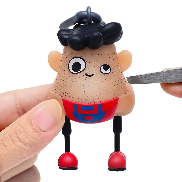 a person holding a pair of scissors in front of a small toy with a face on it