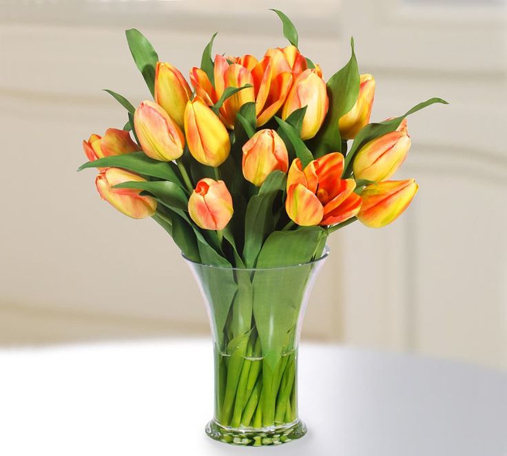 a vase filled with orange and yellow tulips on top of a white table