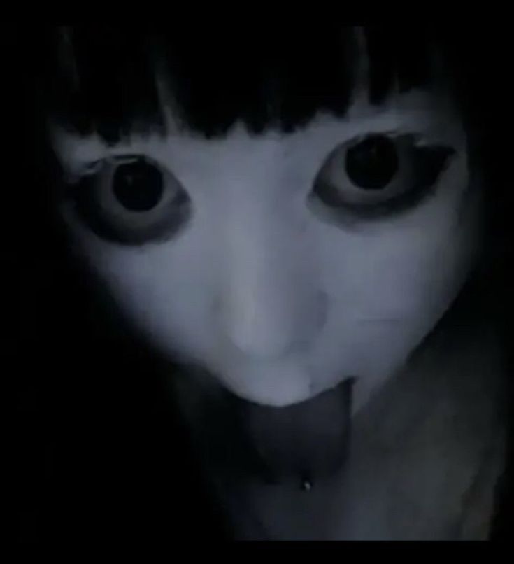 a creepy woman with her tongue out in the dark