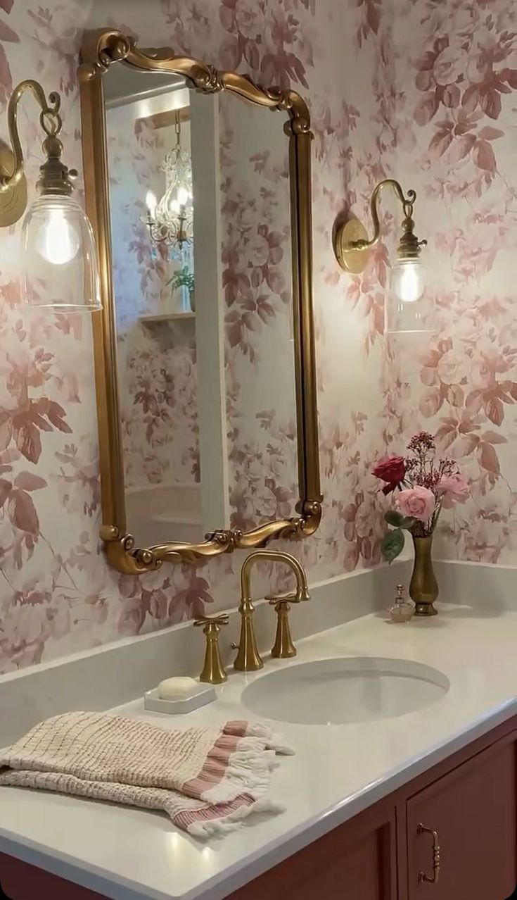 a bathroom sink with a large mirror above it and pink flowers on the wall behind it