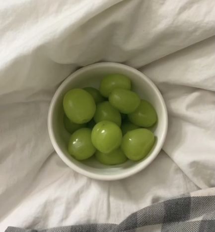 a white bowl filled with green grapes on top of a bed