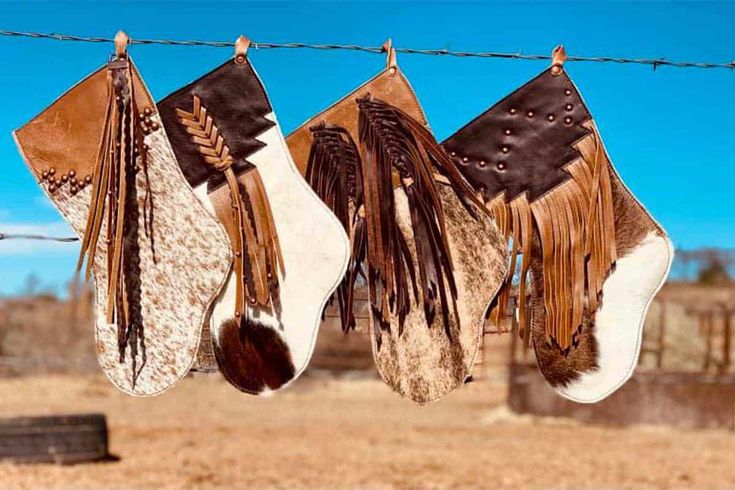 three brown and white feathers hanging from a line on a barbed wire with a barn in the background