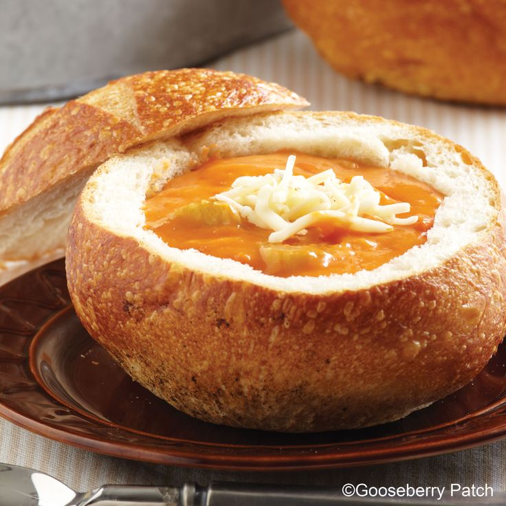 a close up of a bowl of soup on a plate with bread in the background