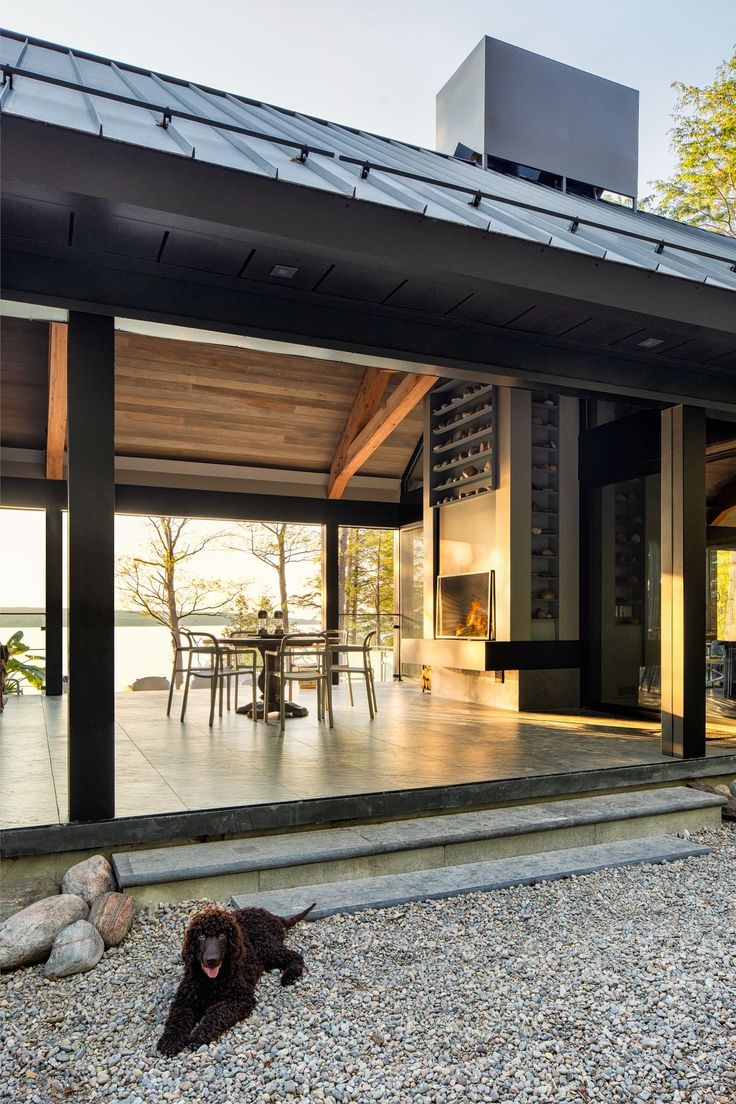 a black dog laying on the ground in front of a house with glass doors and windows