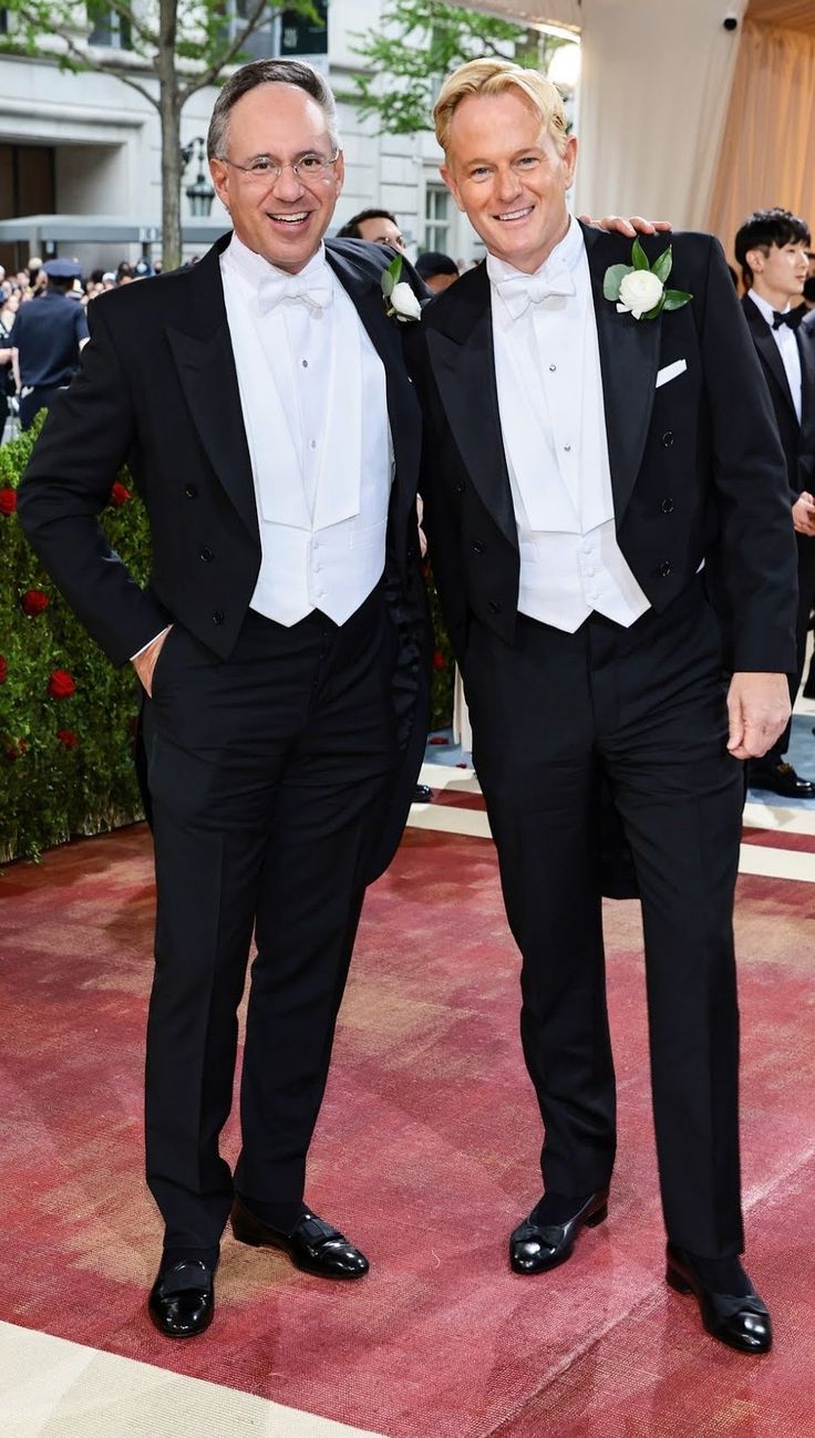 two men in tuxedos standing next to each other on the red carpet at an event