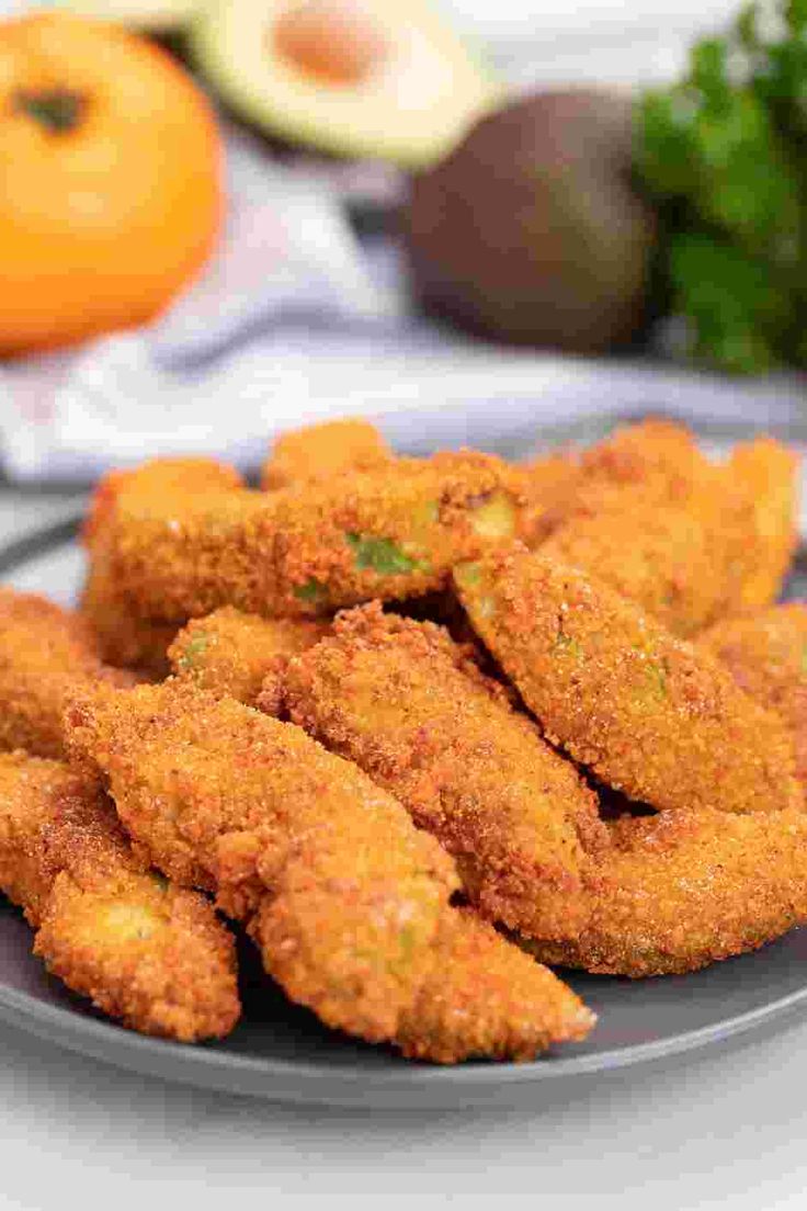 fried chicken nuggets on a plate next to an orange and other vegetables in the background