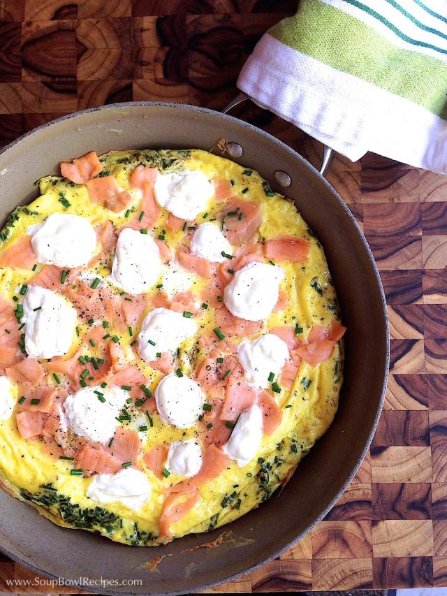 an omelet with salmon, cheese and herbs in a skillet on a wooden table