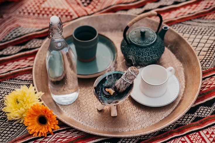 a tray with tea cups and saucers sitting on top of a table next to an orange flower