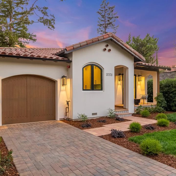 a white house with brown garage doors and brick walkway leading to the front door at dusk