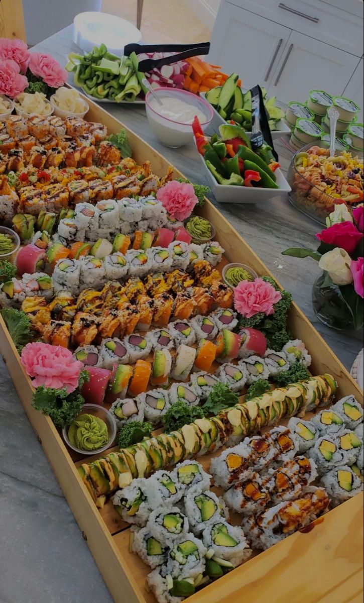 an assortment of sushi on display in a wooden tray at a buffet table with other food items