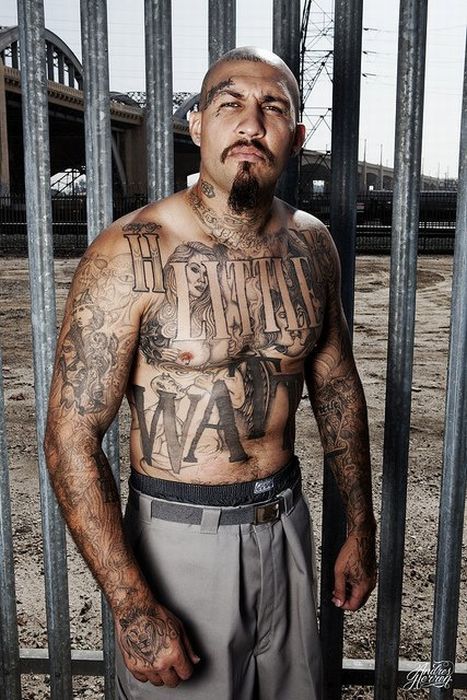 a man standing in front of a jail cell with tattoos on his chest and arms