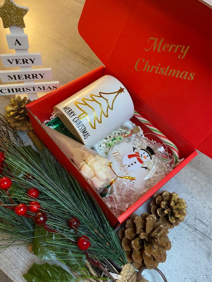 a red box filled with assorted christmas items next to pine cones and other holiday decorations