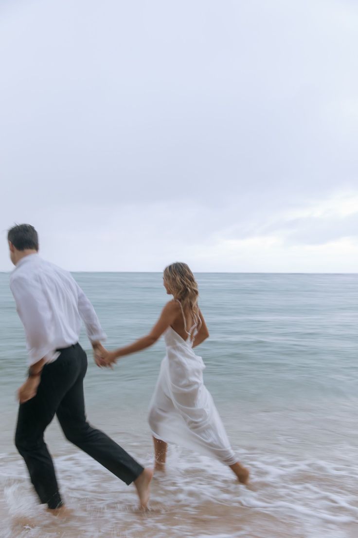 a man and woman holding hands while walking in the ocean