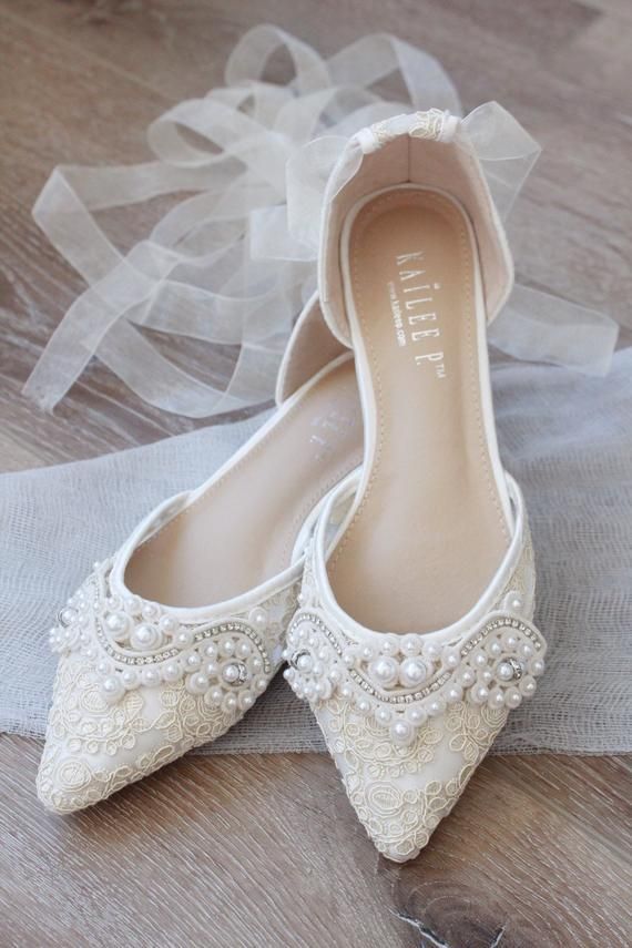 white wedding shoes with pearls on them sitting on top of a wooden floor next to a veil