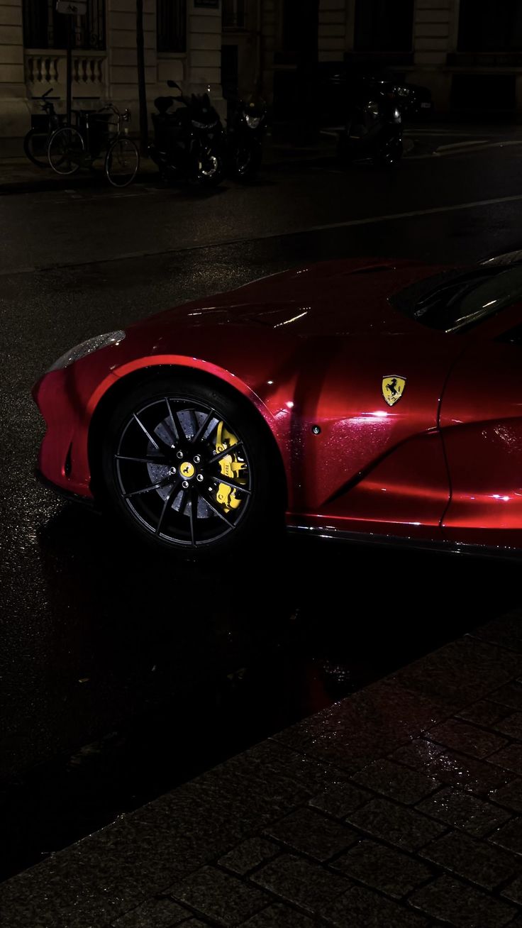 a red sports car is parked on the side of the road at night with its lights on