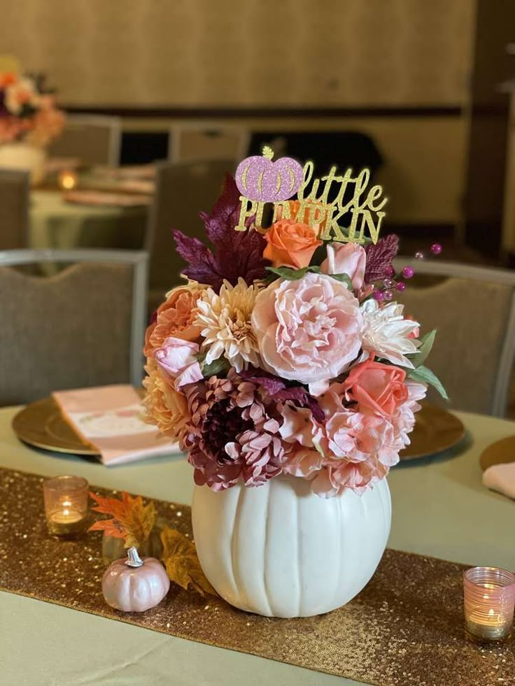 a white pumpkin shaped vase filled with flowers on top of a gold table cloth covered table