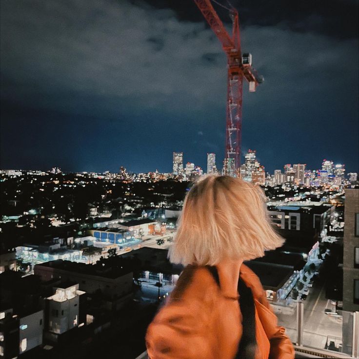 a woman standing on top of a building next to a tall crane in the city