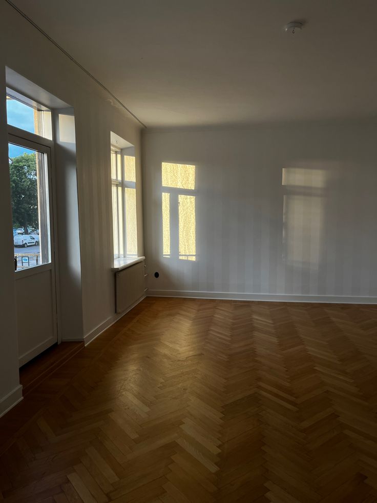 an empty room with wooden floors and two large windows in it's center wall