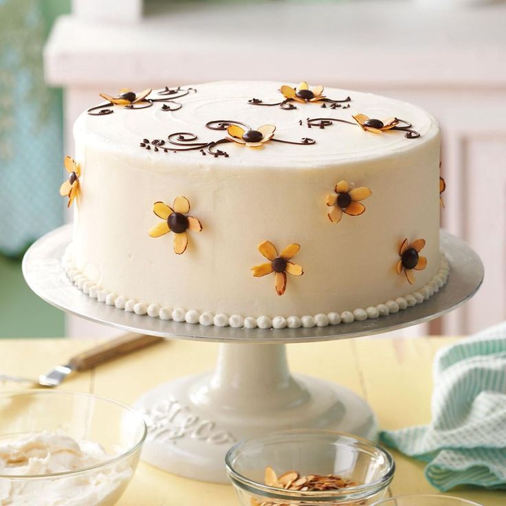 a white cake with yellow flowers on it sitting on a table next to a glass bowl