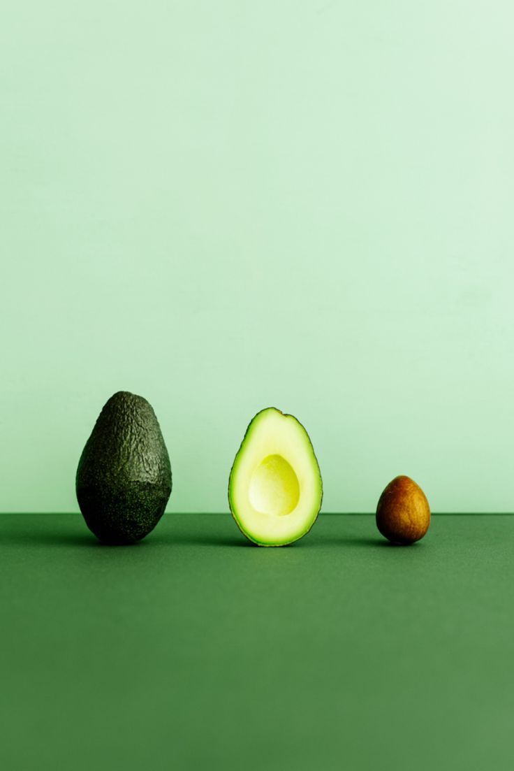 an avocado and two other fruits on a green surface