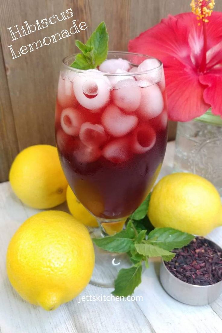 a glass filled with liquid next to lemons and flowers