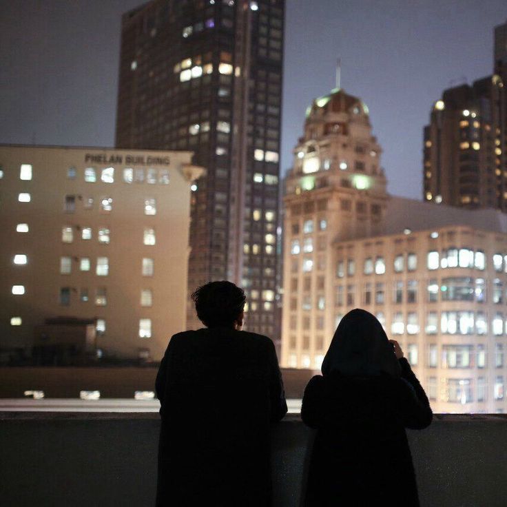 two people are looking out over the city at night with skyscrapers in the background