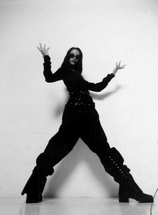 a woman in black is posing with her arms out and legs spread wide as she stands on one leg