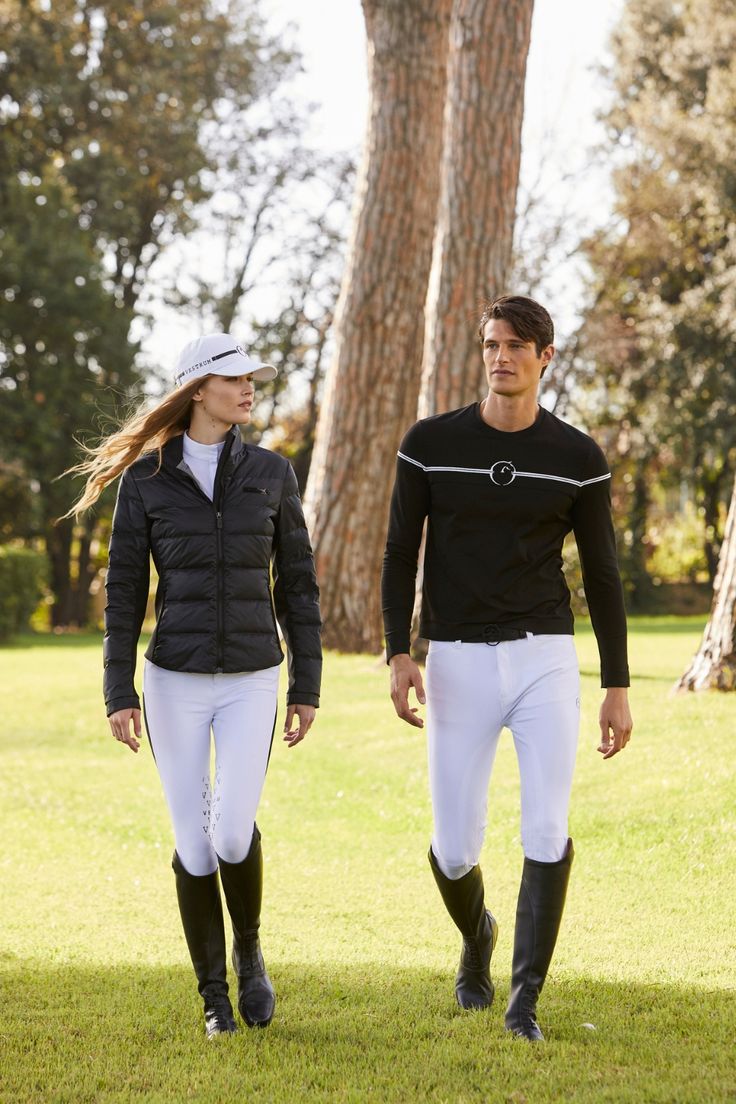 a man and woman in riding gear walking through the grass with trees in the background