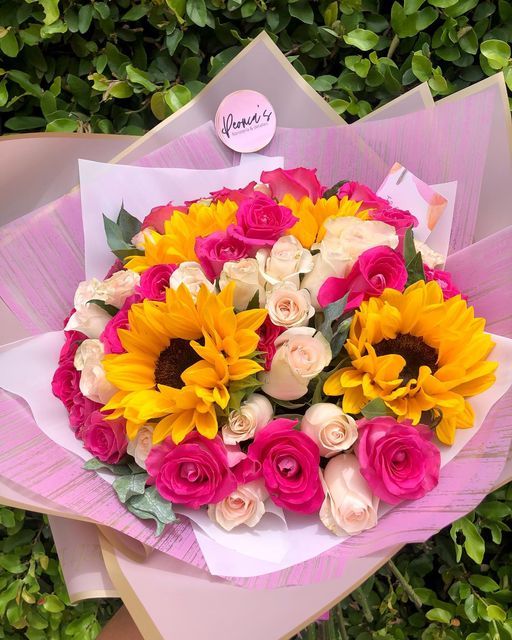 a bouquet of sunflowers and roses is wrapped in pink paper