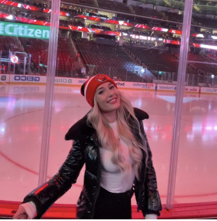 a woman standing in front of an ice rink wearing a red hat and black jacket