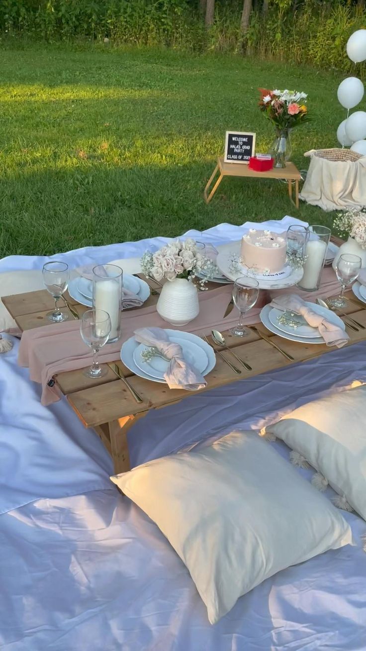 a table set up for a party with white plates and candles on it in the grass