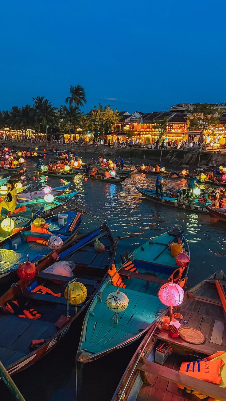 many small boats are lined up in the water at night with colorful lights on them